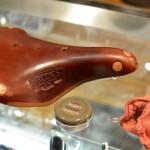 Close-up of a Brooks leather bicycle seat and a tin of Proofide leather dressing