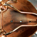 Close-up of a copper-toned object with wire framework and small holes.