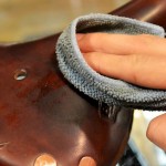 A hand is wiping a brown leather cycle seat with a gray cloth