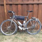 A bicycle with attached bags and water bottles, leaning against a wooden fence