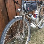 A muddy bicycle with gear attached is parked against a wooden fence