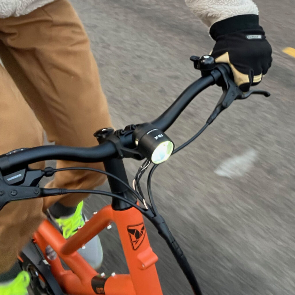 A person riding an orange bike outdoors with a headlight shining.