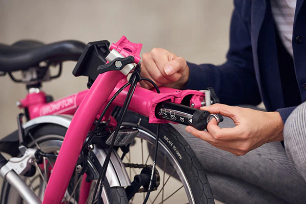 Folded pink Brompton bike, showing person pulling toolkit out of its place within the frame.