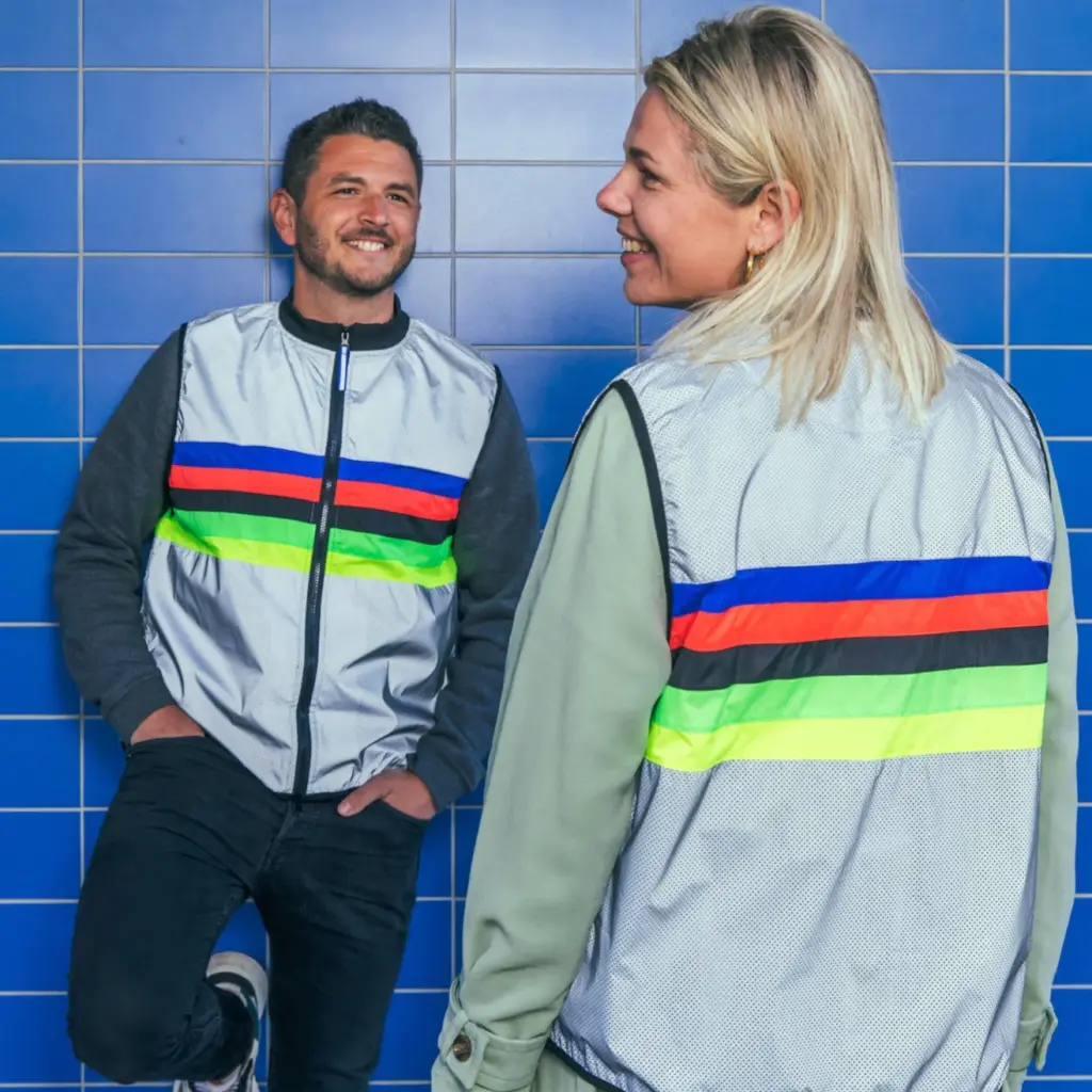 Two smiling people face each other wearing rainbow safety vests.